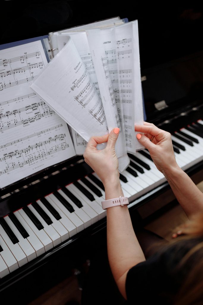 Close-up view of hands flipping through sheet music on a piano, emphasizing musical practice.