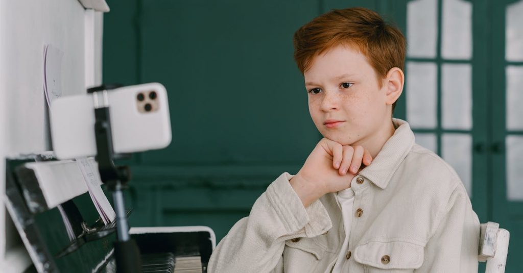 A focused young boy takes piano lessons online, showcasing the blend of education and music at home.